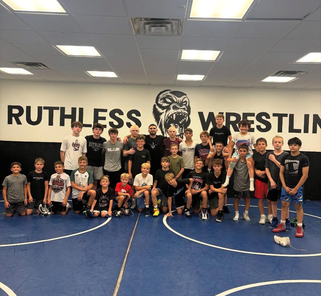 Ruthless Wrestling Club middle school wrestling team gathered in the training room under the wall logo